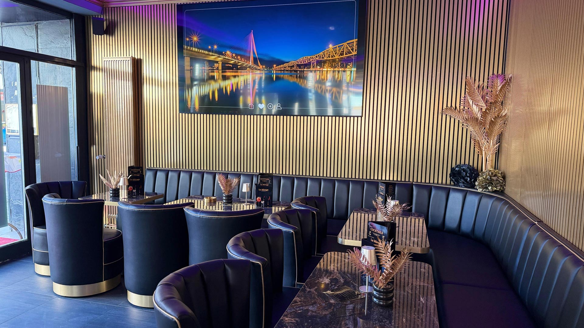 Schicker Lounge Bereich mit schwarzen Ledersofas und goldenen Akzenten vor einem großen Bild einer beleuchteten Brücke