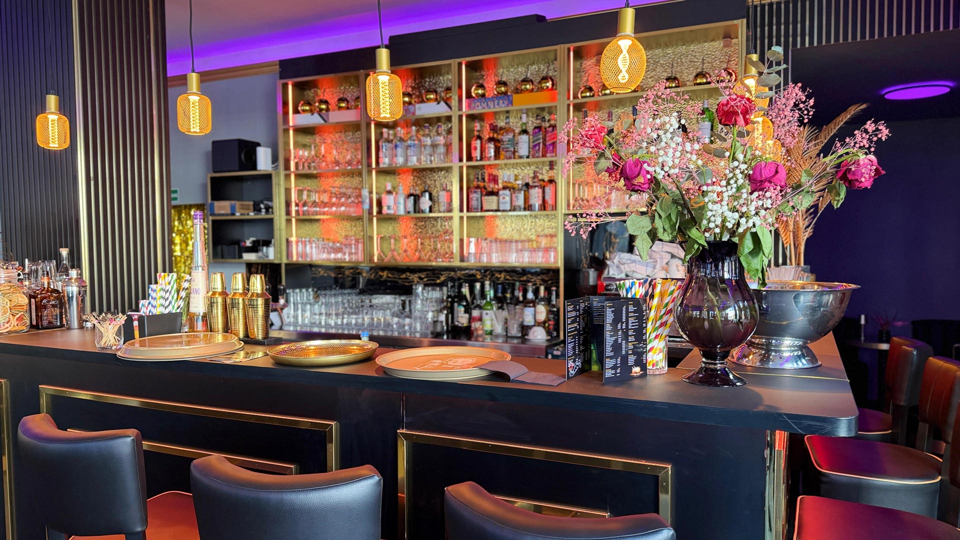 Eine stilvolle Bar mit schwarzen und goldenen Akzenten und bunten Blumenarrangements