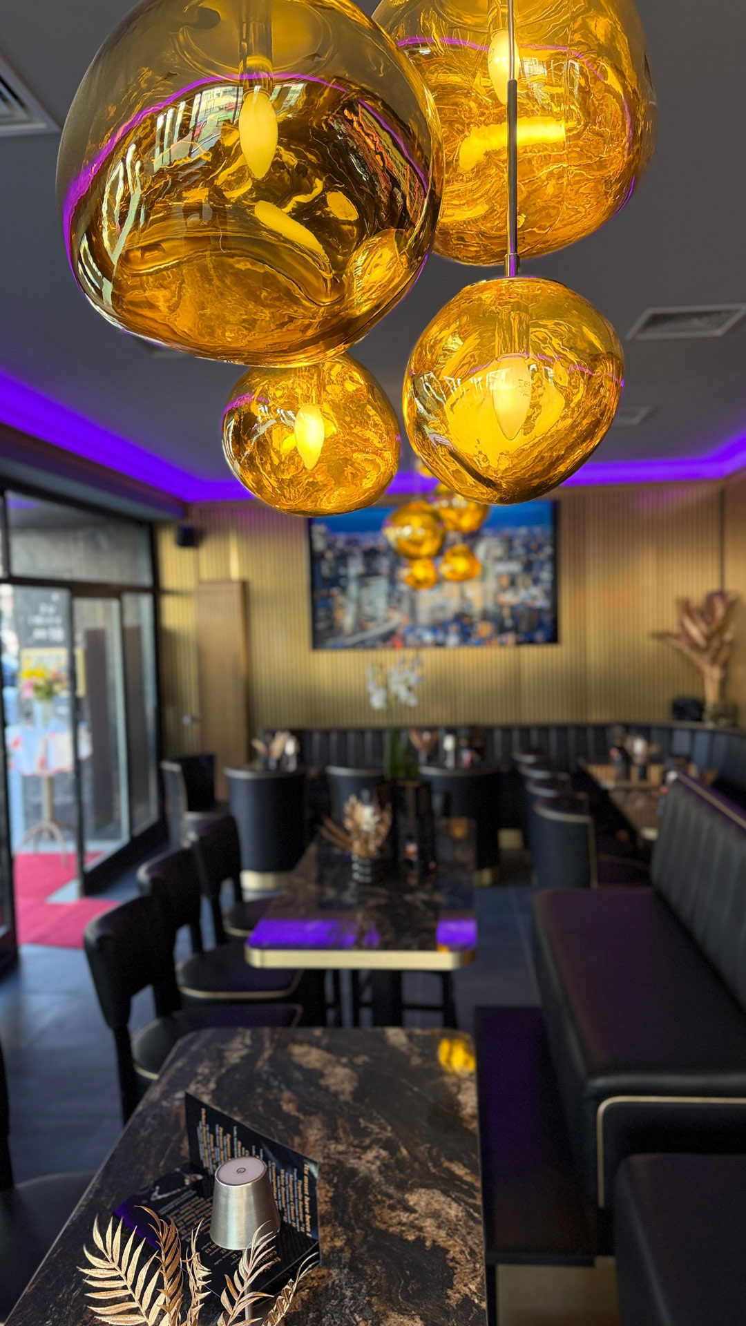 Elegantes Restaurant mit goldenen Lampen, lila Beleuchtung und dunklen Möbeln