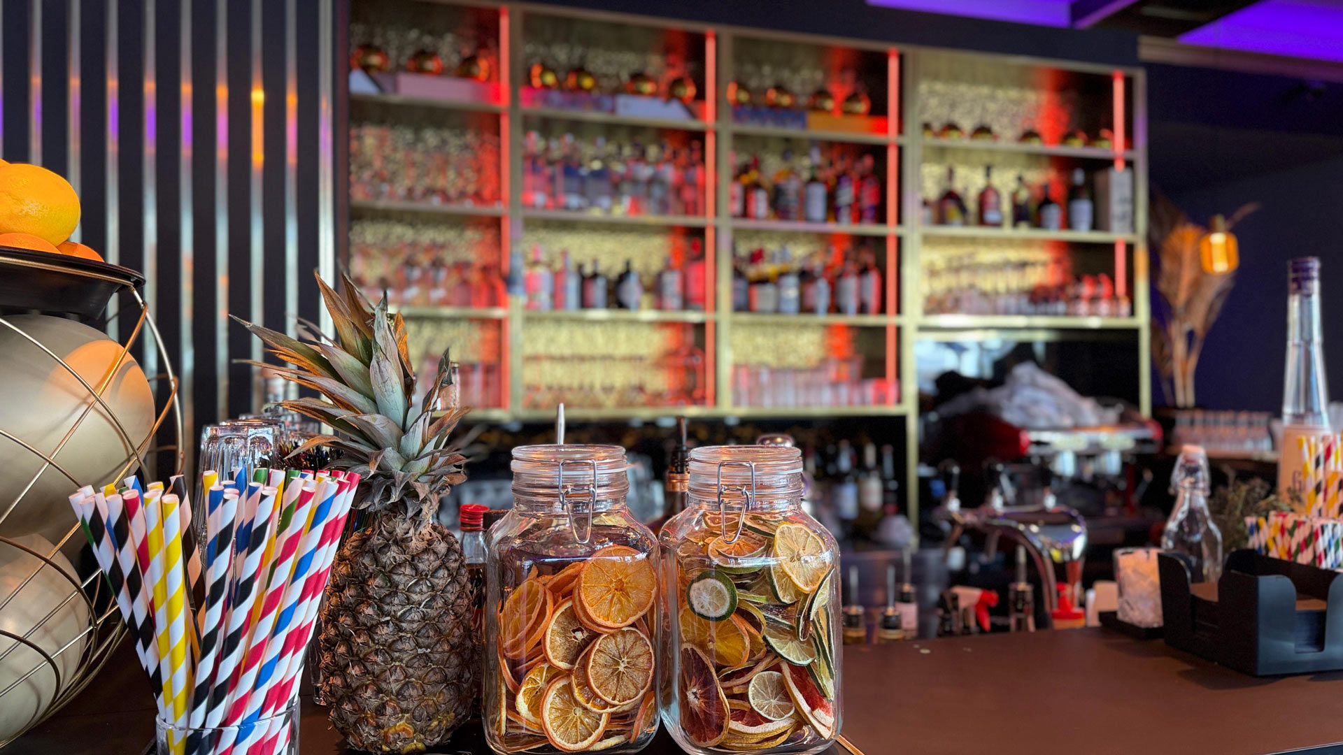 Bunte Bar mit Trockenfruechten in Glaesern, einer Ananas und gestreiften Strohhalmen